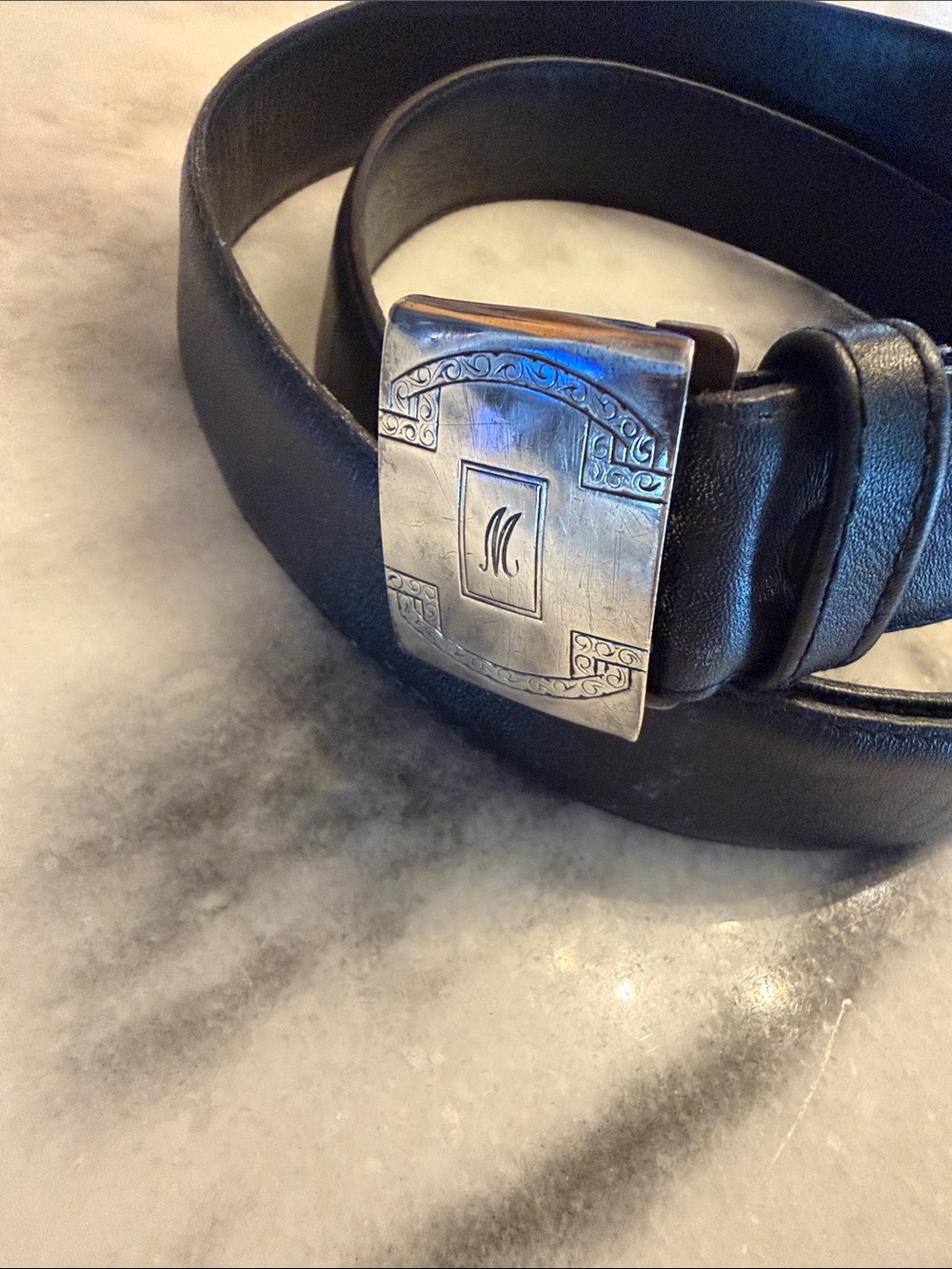Sterling silver belt buckle monogrammed “M” on a black leather belt. Size adjust